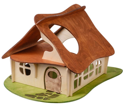A medium-sized wooden dollhouse with a thatched roof and multiple windows, set on a green base that represents grass.