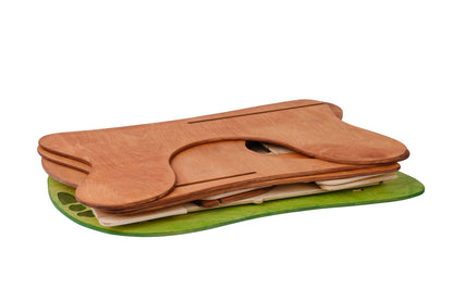 Unassembled two-story wooden dollhouse with a brown slotted roof, beige walls, and green accents representing grass at the base. 